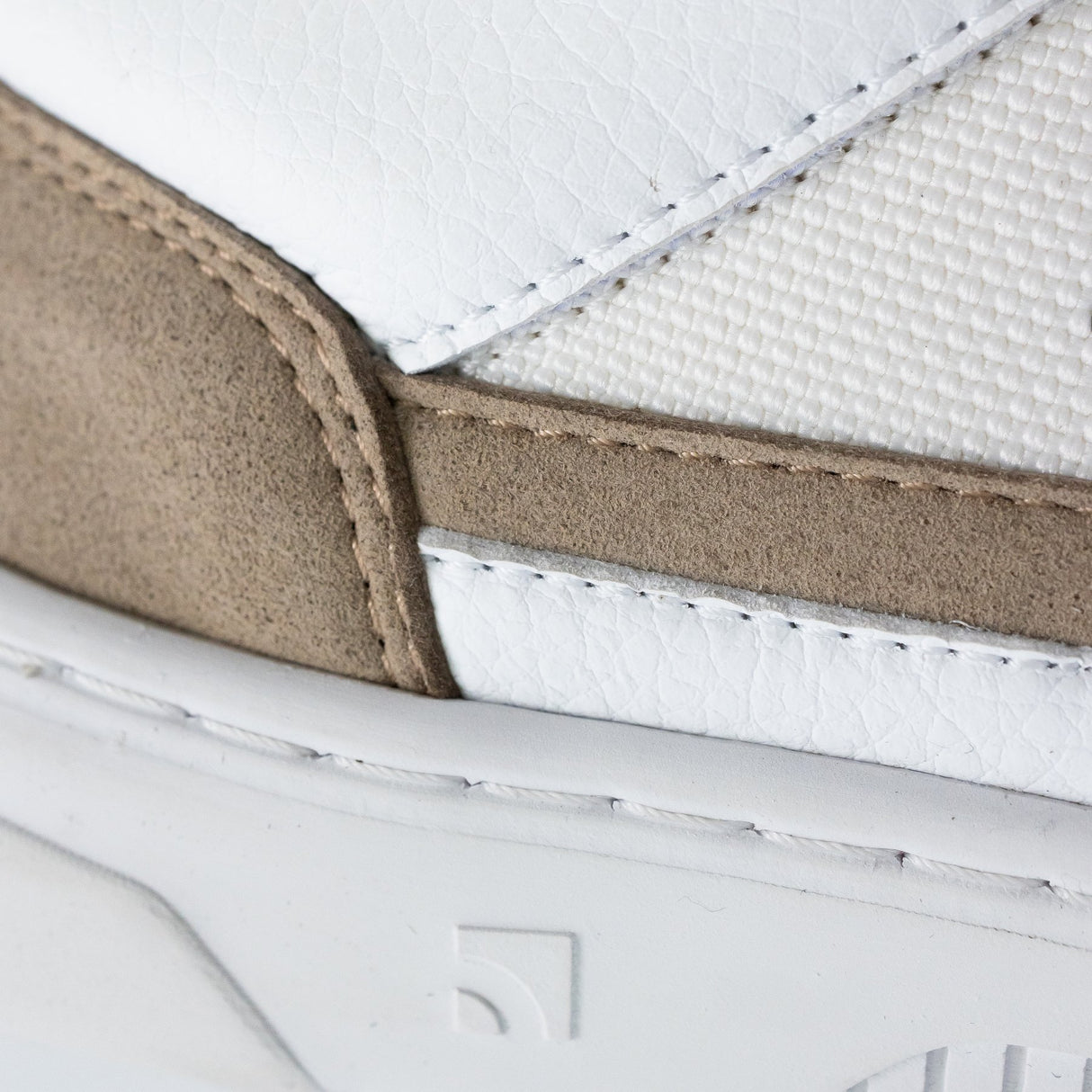 Close-up of white sneaker with beige suede accents and textured white fabric panel.