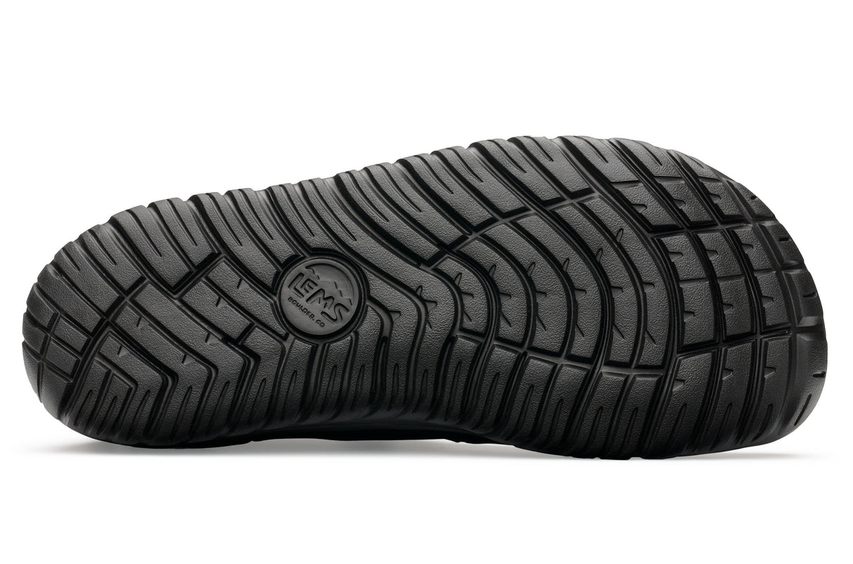 Black rubber sole of Lems Chelsea Boot with deep grooves and circular logo embossed in center.