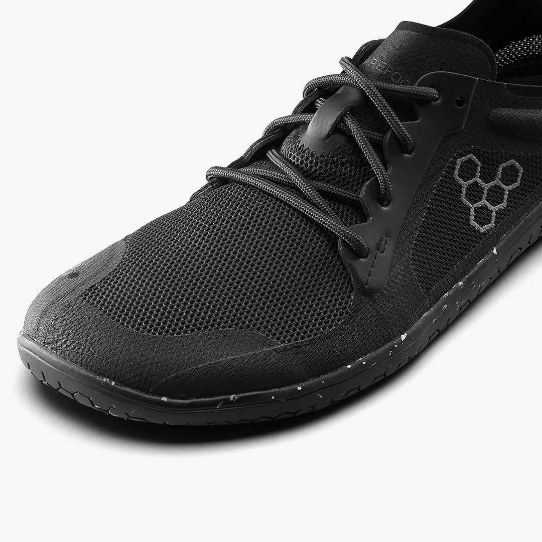 Close-up of black breathable mesh Vivobarefoot athletic shoe with minimalist sole and hexagonal logo on side.