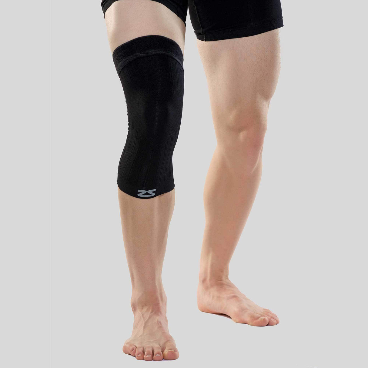 Black compression knee sleeve on left leg, fitted snugly from mid-thigh to below the knee.