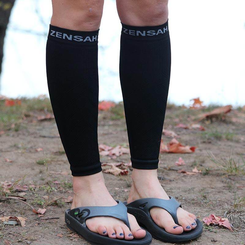 Black Zensah compression leg sleeves worn on calves with brand name at top, paired with black sandals.