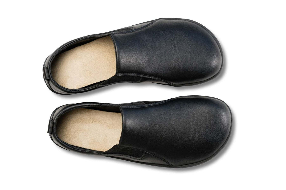 Black slip-on sneakers in vegan leather with a smooth finish and rounded toe, viewed from above.