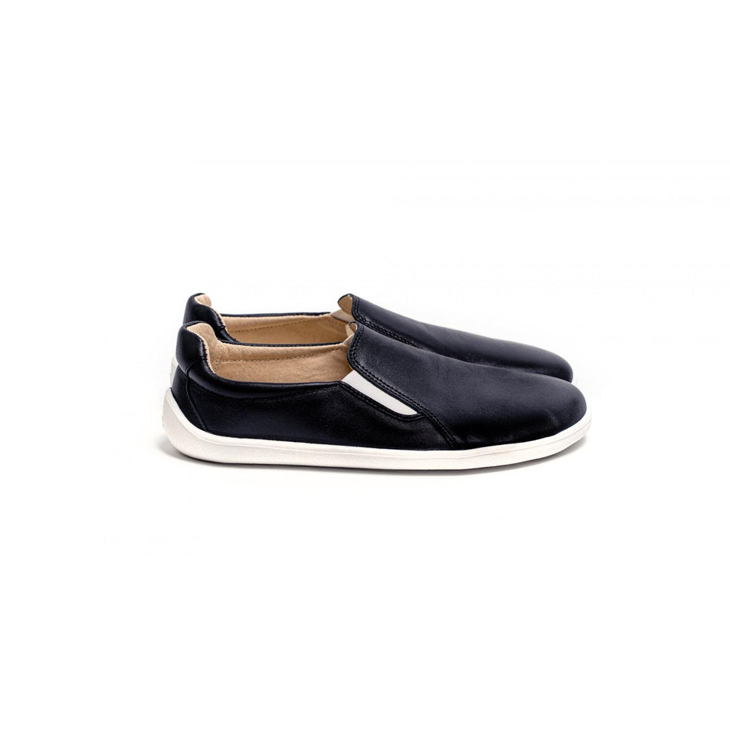 Black slip-on casual shoes with white soles and tan inner lining, minimalist design.