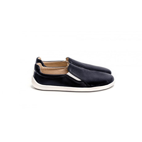 Black slip-on casual shoes with white soles and tan inner lining, minimalist design.