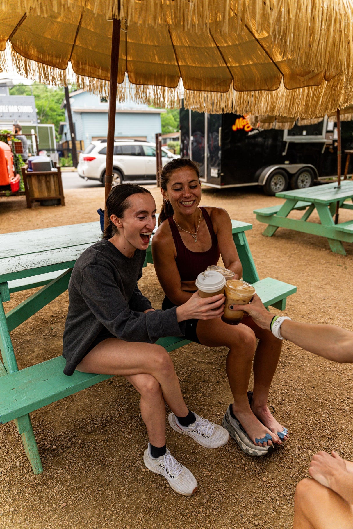 Mauve Correct Toes SPORT® toe spacers worn on bare feet, shown outdoors with people sitting on a green bench under a straw.