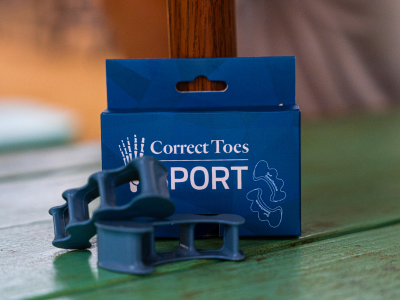Mauve silicone toe spacers next to blue Correct Toes SPORT® box on green surface.