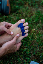 Blue Correct Toes SPORT toe spacers worn on bare foot, held by hands outdoors on grass background.