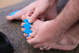 Aqua toe spacers placed between toes on bare feet against a rough asphalt surface.