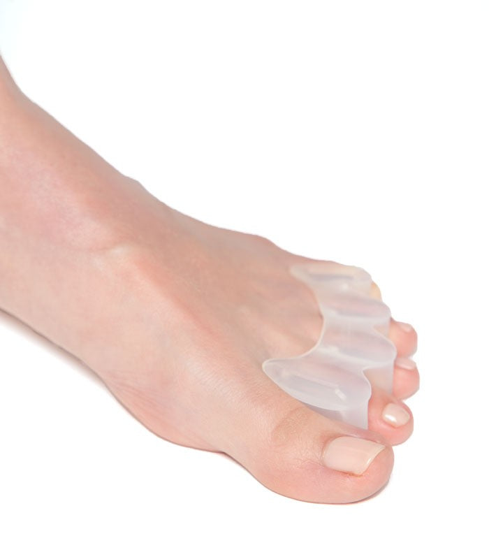 Transparent silicone toe spacer worn between toes on bare foot.