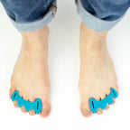 Aqua-colored Correct Toes toe spacers worn on bare feet with rolled-up denim jeans.