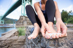 Bare feet with aqua-colored Correct Toes original toe spacers on each toe, outdoor background with bridge and water.