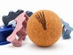 A cork massage ball with a black foot print graphic, shown alongside pink, blue, and gray plastic foot-shaped massage tools on a white background.