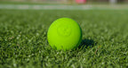 Bright green Fascia Friend lacrosse ball with embossed logo on grass background.