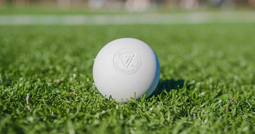 White Fascia Friend Lacrosse Ball with embossed logo on green grass field.