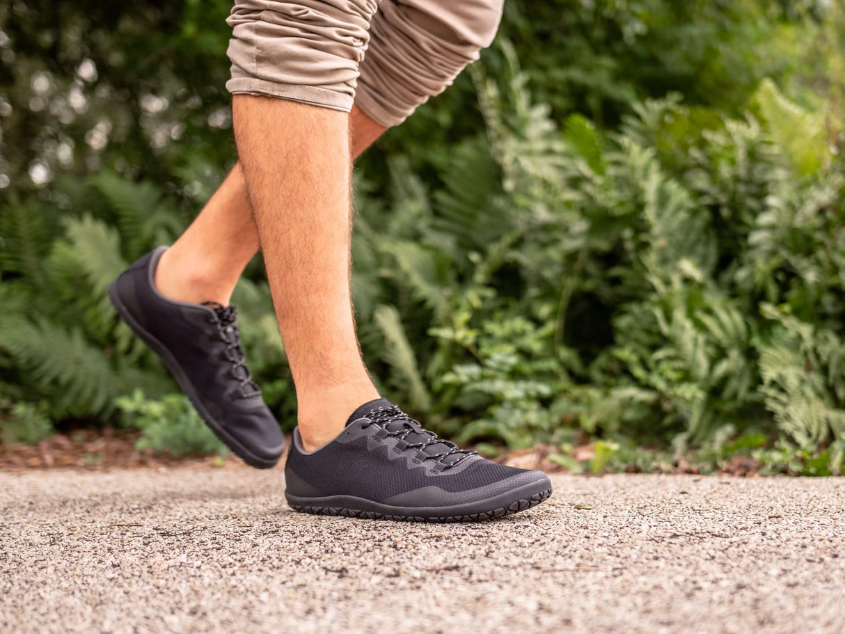 Black athletic sneakers with low profile design, textured sole, and mesh upper worn outdoors.