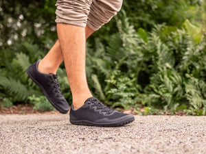 Black athletic sneakers with low profile design, textured sole, and mesh upper worn outdoors.