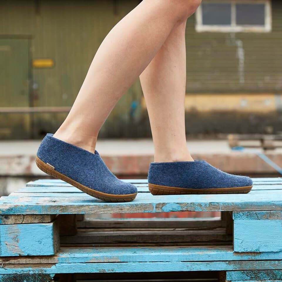 Denim blue slip-on shoes with honey-colored natural rubber soles worn on feet outdoors.