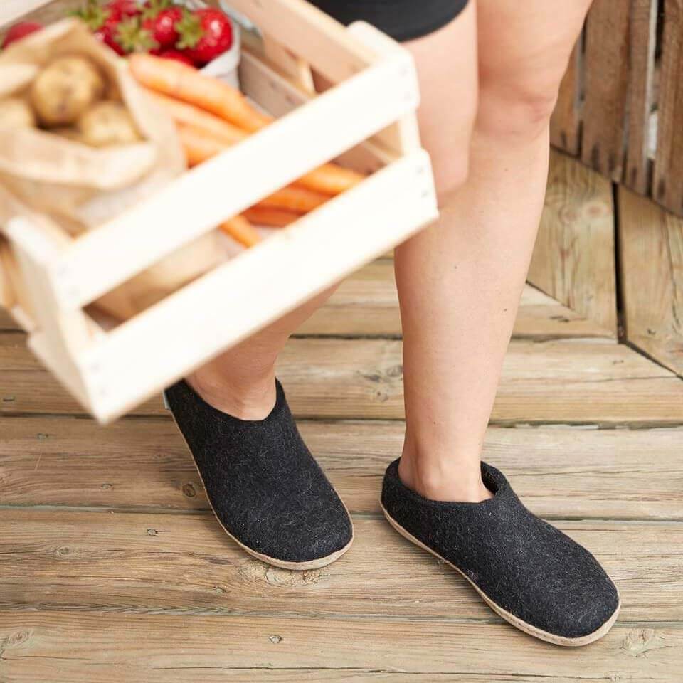 Charcoal gray slip-on slippers with leather soles worn on wooden porch floor.