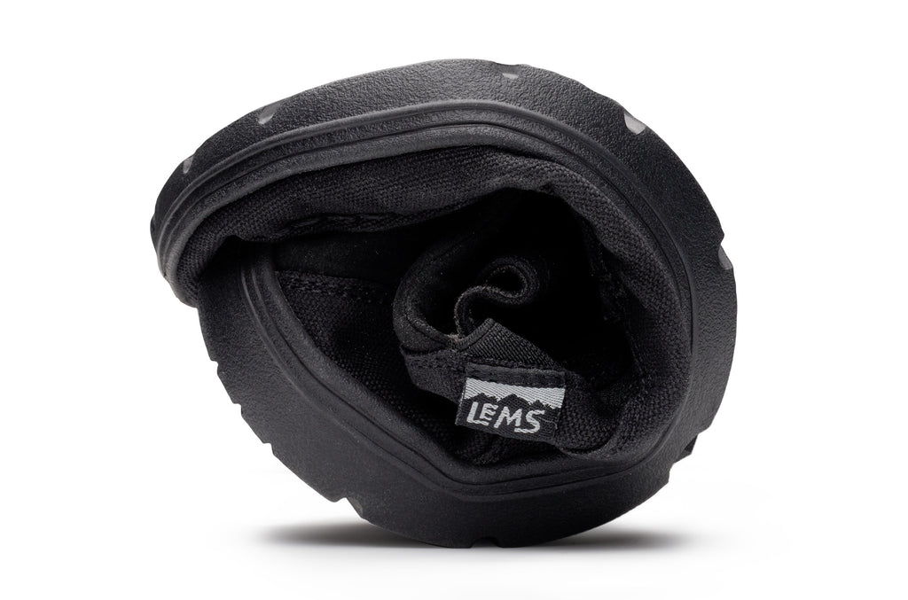 Black flexible Lems Drifter casual shoe folded to show its pliable sole and interior lining.