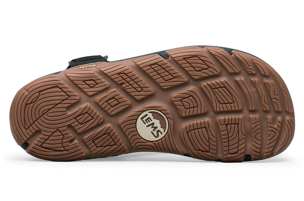 Brown rubber sole of Lems Switchback sandal with deep tread pattern and Lems logo in the center.