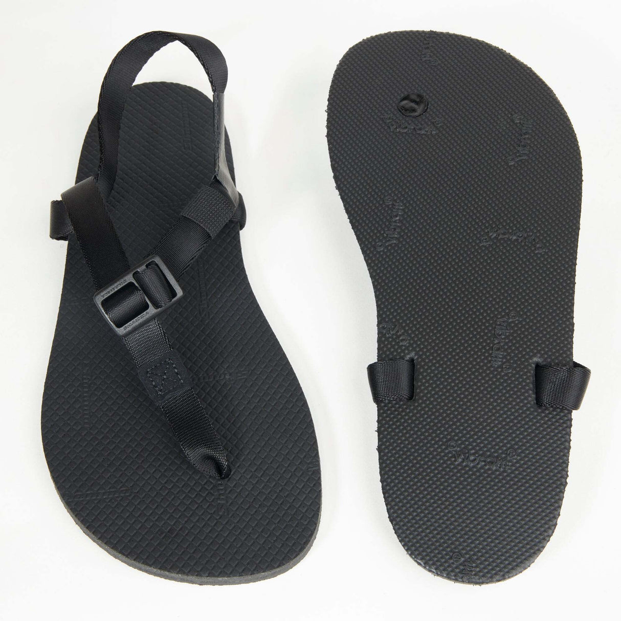 Black minimalist sandal with adjustable buckle strap and textured sole, paired with matching smooth outsole.