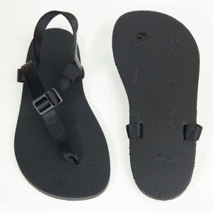 Black minimalist sandal with adjustable buckle strap and textured sole, paired with matching smooth outsole.