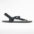 Black minimalist flat sandal with adjustable strap and toe loop on textured sole.