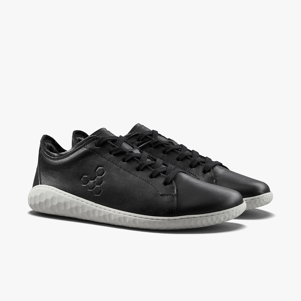 Black leather low-top sneakers with white textured soles and subtle logo on the side.