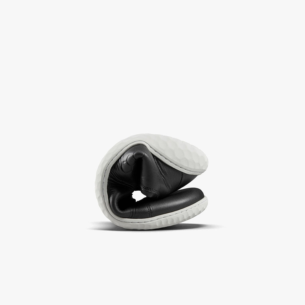 Black leather minimalist shoe folded to show flexibility with white textured sole.