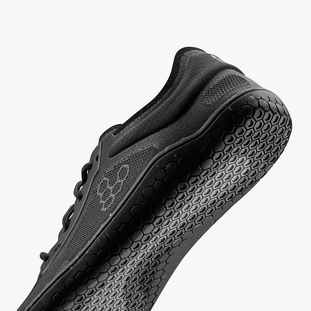 Black low-profile athletic shoe with textured honeycomb sole and sleek mesh upper.