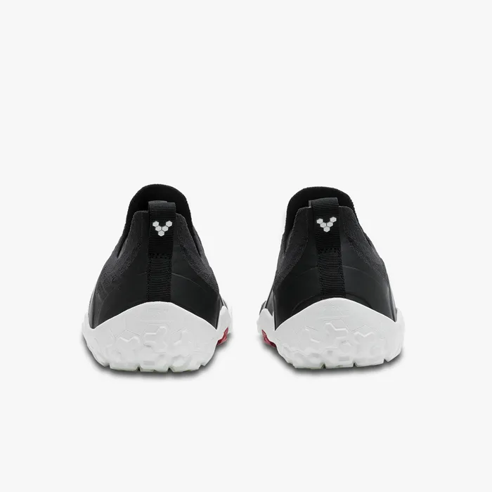 Pair of black Vivobarefoot Primus Trail Knit FG shoes shown from the back with white textured soles and red accents.