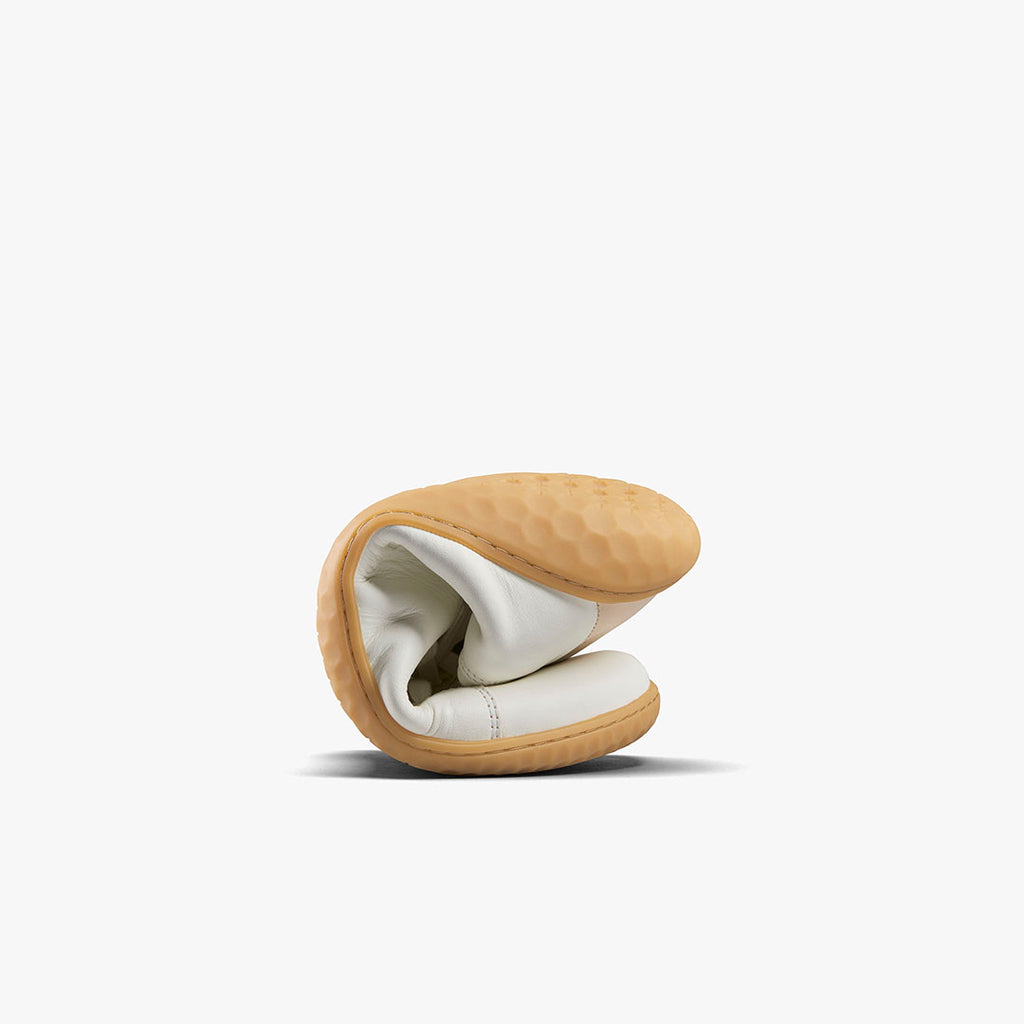 Flexible white and rose leather sneaker folded to show its soft, tan sole with textured grip pattern.