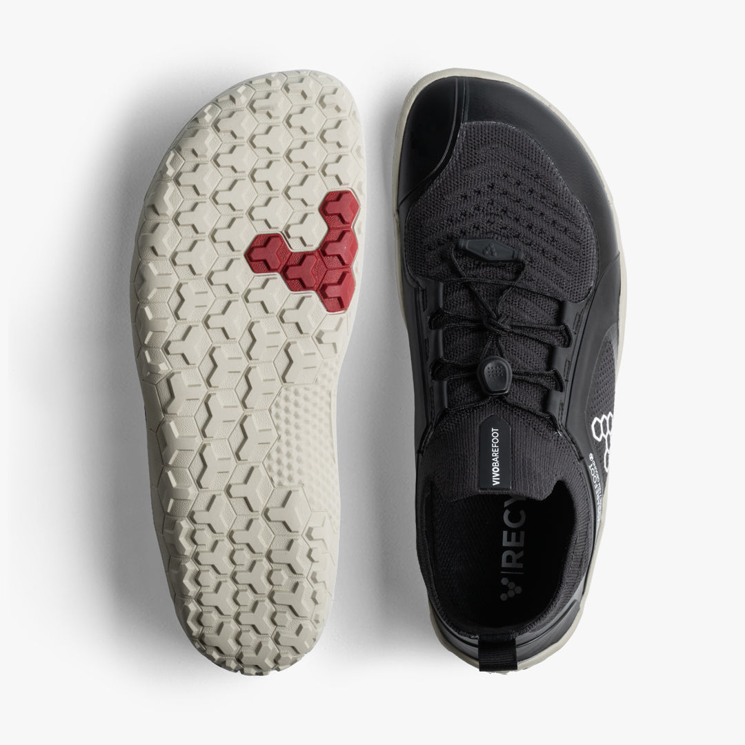 Black knit low-profile athletic shoe with white textured sole and red hexagonal tread accents.