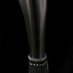 Black and grey XOTOES™ 5.0 anklet with neon green accents on a black mannequin leg against black background.