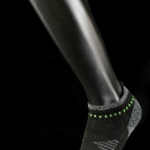 Black and grey ankle sock with neon green accent dots on the cuff, worn on foot mannequin against black background.
