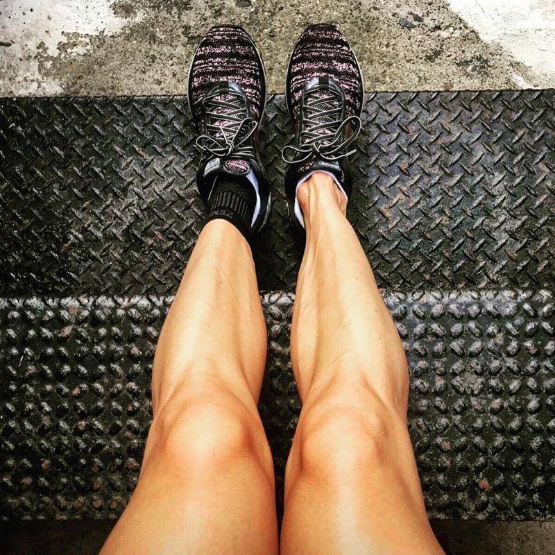 Black compression ankle sleeves worn on legs with black and pink running shoes on textured surface.