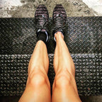 Black compression ankle sleeves worn on legs with black and pink running shoes on textured surface.