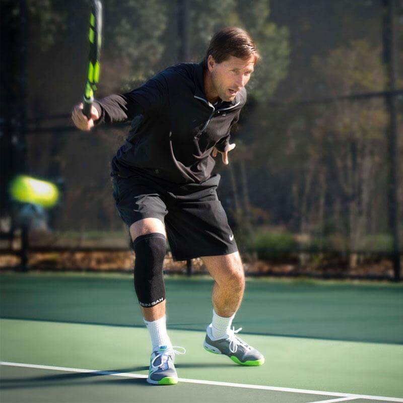 Black compression knee sleeves worn by male tennis player on green court.