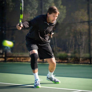 Black compression knee sleeves worn by male tennis player on green court.