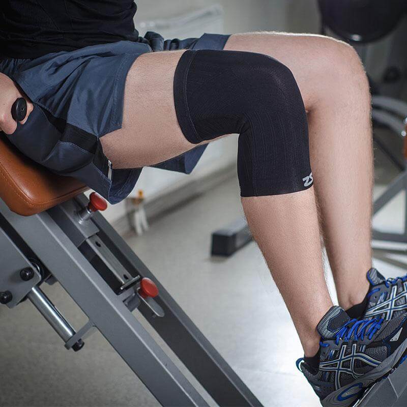Black compression knee sleeves worn on both legs, made of smooth stretchy fabric with a small white logo near the knee.