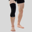 Black compression knee sleeve on left leg, fitted snugly from mid-thigh to below the knee.