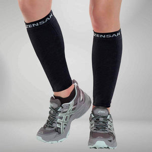 Black knee-high compression leg sleeves with white Zensah logo worn with gray running shoes.