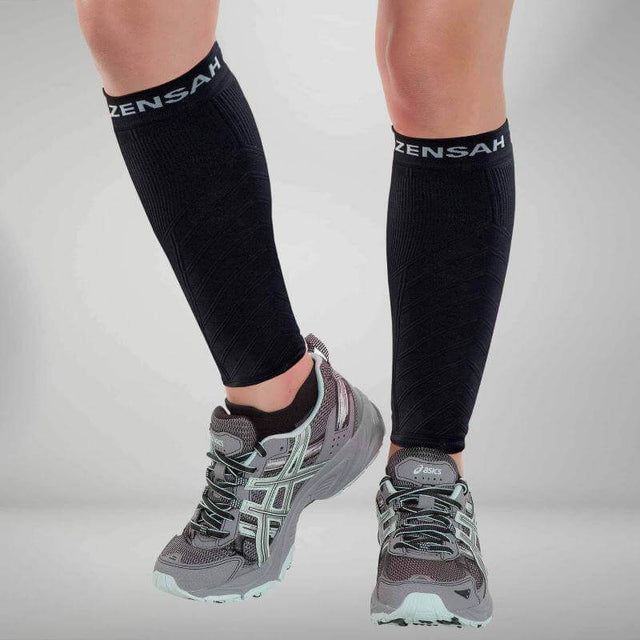 Black knee-high compression leg sleeves with white Zensah logo worn with gray running shoes.
